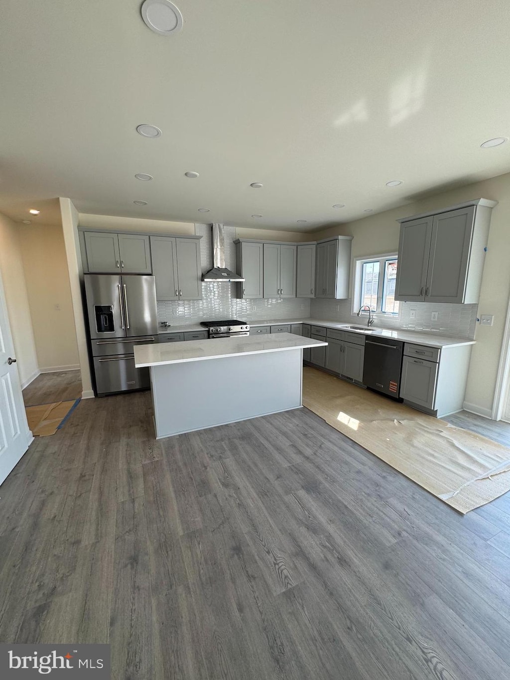 kitchen featuring gray cabinets, tasteful backsplash, stainless steel appliances, wall chimney exhaust hood, and light countertops