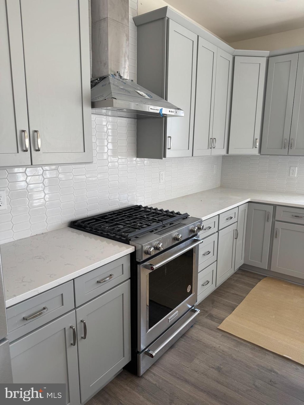 kitchen with tasteful backsplash, wall chimney range hood, dark wood finished floors, gray cabinets, and high end stainless steel range oven