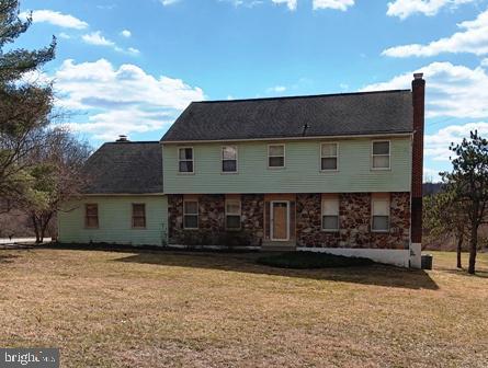 rear view of property featuring stone siding, a lawn, and a chimney