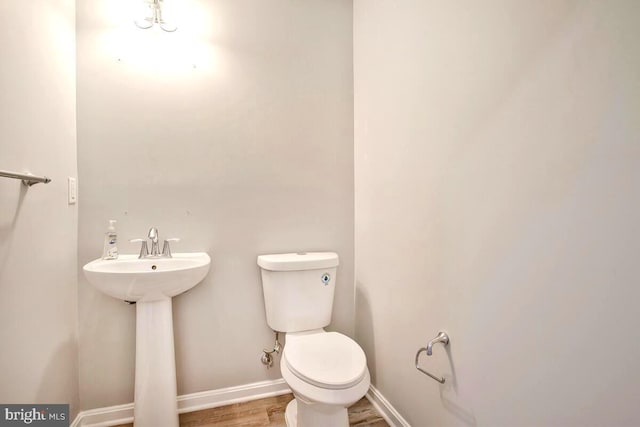 half bath featuring a sink, toilet, baseboards, and wood finished floors