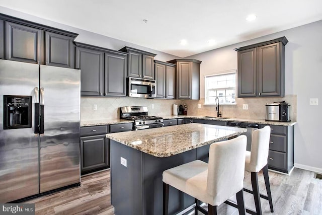 kitchen with light stone counters, light wood finished floors, a breakfast bar, a sink, and stainless steel appliances