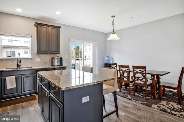 kitchen with wood finished floors, a kitchen island, a breakfast bar, a sink, and decorative backsplash