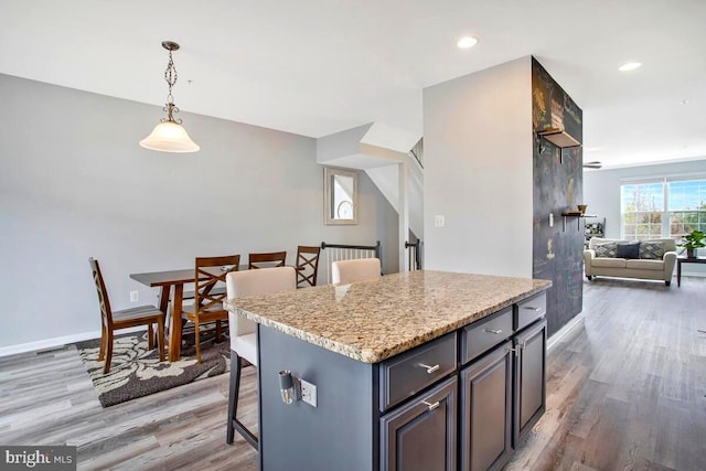 kitchen featuring decorative light fixtures, open floor plan, light wood-style floors, a breakfast bar area, and baseboards