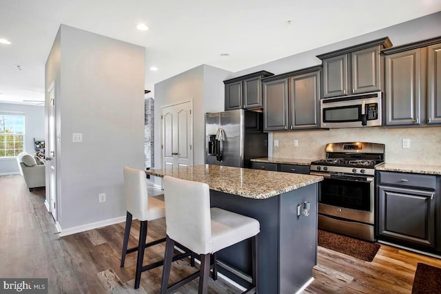 kitchen with dark wood finished floors, a center island, appliances with stainless steel finishes, a breakfast bar area, and decorative backsplash