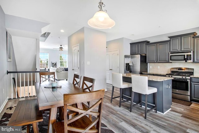 interior space with stainless steel appliances, wood finished floors, ceiling fan, and a center island