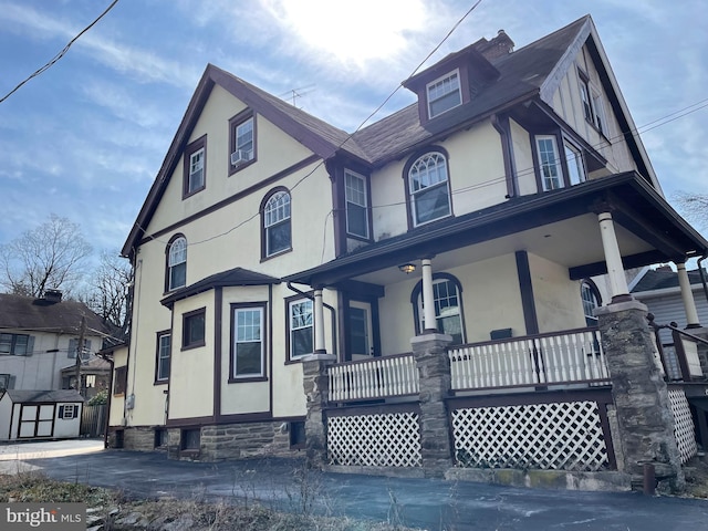 tudor-style house featuring an outbuilding, stucco siding, a porch, and a storage unit