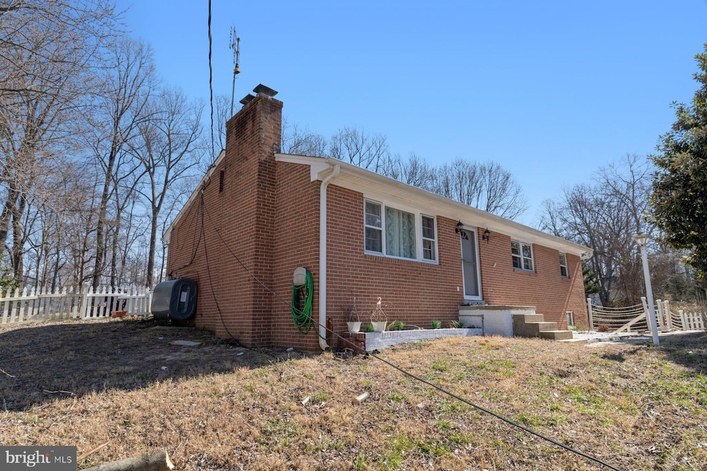 rear view of property with brick siding, a chimney, and fence