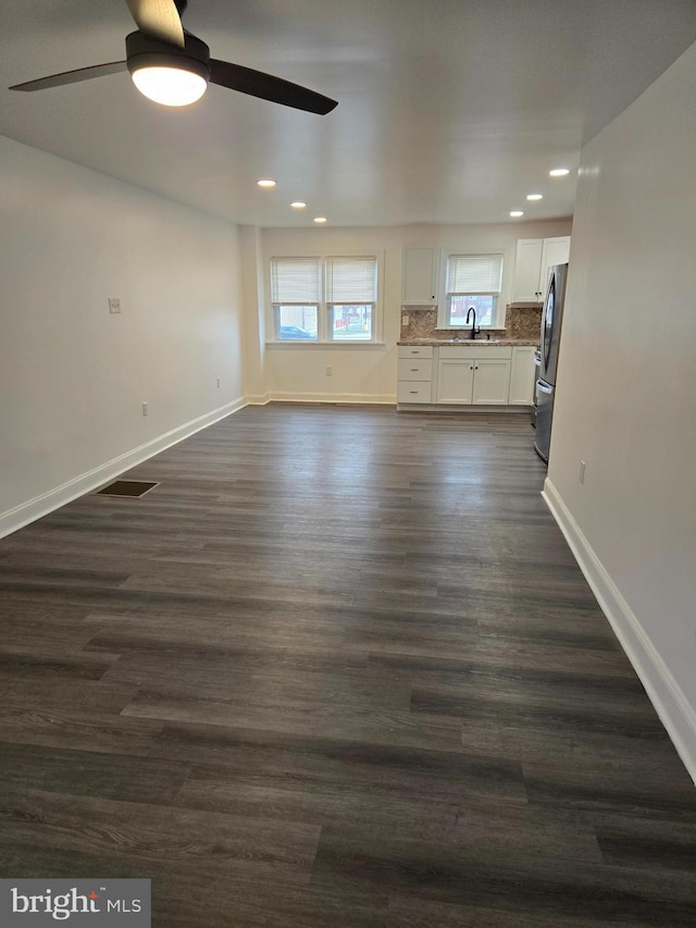 unfurnished living room featuring dark wood-type flooring, a ceiling fan, baseboards, and a sink