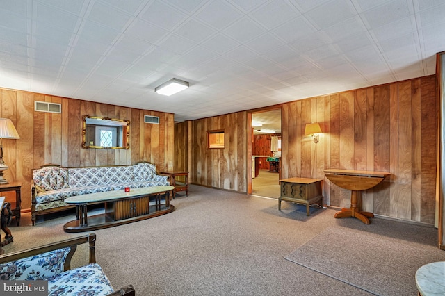 carpeted living room with visible vents and wood walls