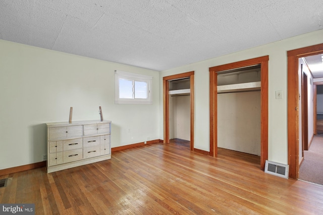 unfurnished bedroom featuring visible vents, multiple closets, a textured ceiling, and hardwood / wood-style floors