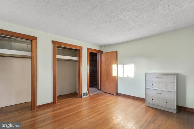 unfurnished bedroom featuring visible vents, a textured ceiling, baseboards, and hardwood / wood-style floors