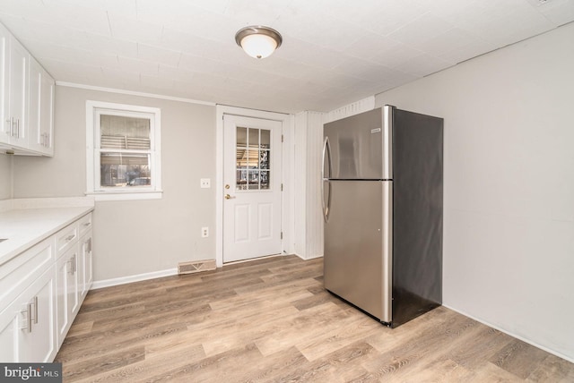 kitchen with white cabinets, light wood-type flooring, freestanding refrigerator, and light countertops