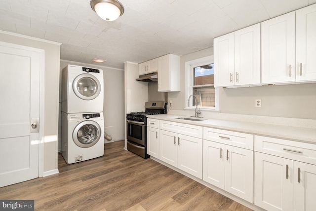 kitchen with a sink, under cabinet range hood, wood finished floors, stacked washer / dryer, and gas range