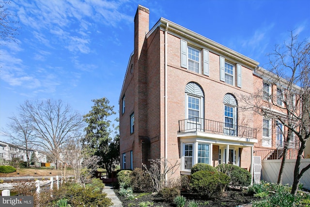 view of front of home with a balcony, fence, brick siding, and a chimney