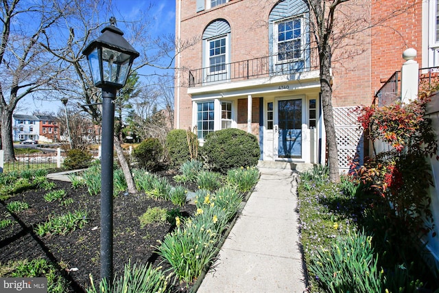 view of exterior entry with a balcony, fence, and brick siding