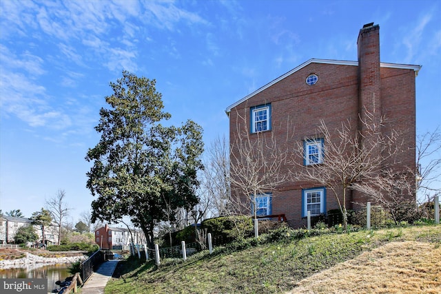 view of property exterior featuring brick siding, a chimney, and fence