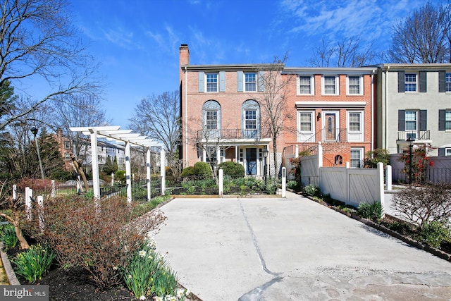 townhome / multi-family property featuring brick siding, a pergola, a fenced front yard, and a chimney