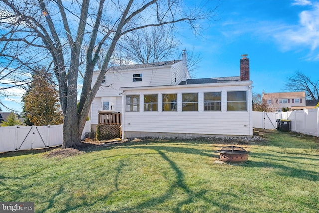 rear view of house featuring a lawn, a fire pit, a fenced backyard, and a gate