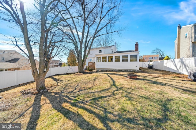 rear view of house with a fire pit, a sunroom, a chimney, a yard, and a fenced backyard