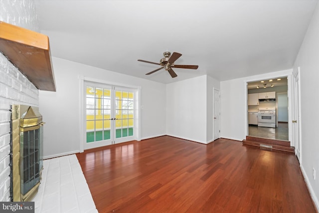 unfurnished living room with a brick fireplace, baseboards, ceiling fan, and dark wood-style flooring