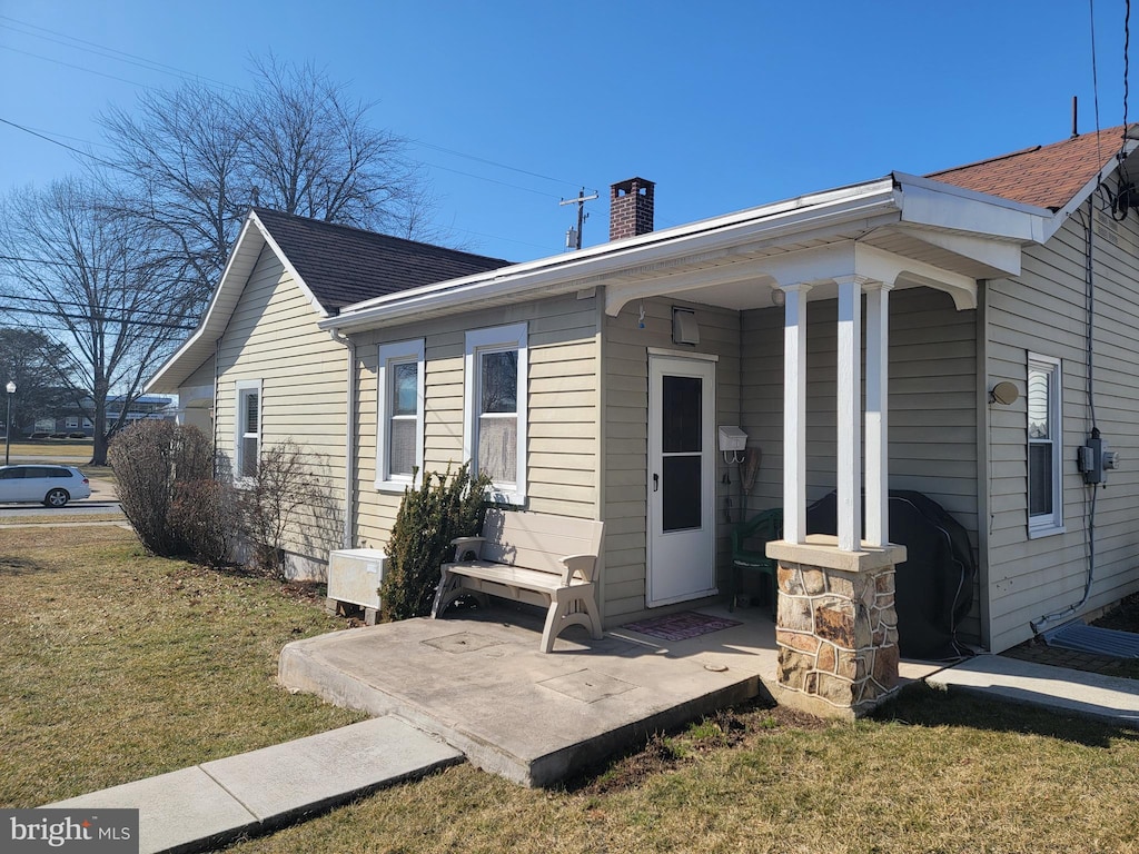 view of front of property featuring a shingled roof, a front lawn, covered porch, and a chimney