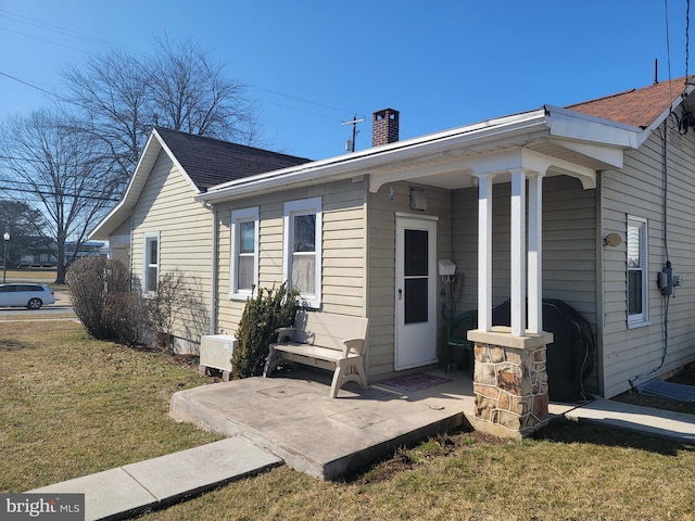 view of front of home with covered porch, a chimney, and a front lawn