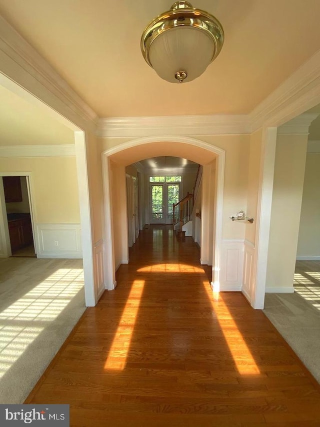 hall with arched walkways, a decorative wall, french doors, and wood finished floors