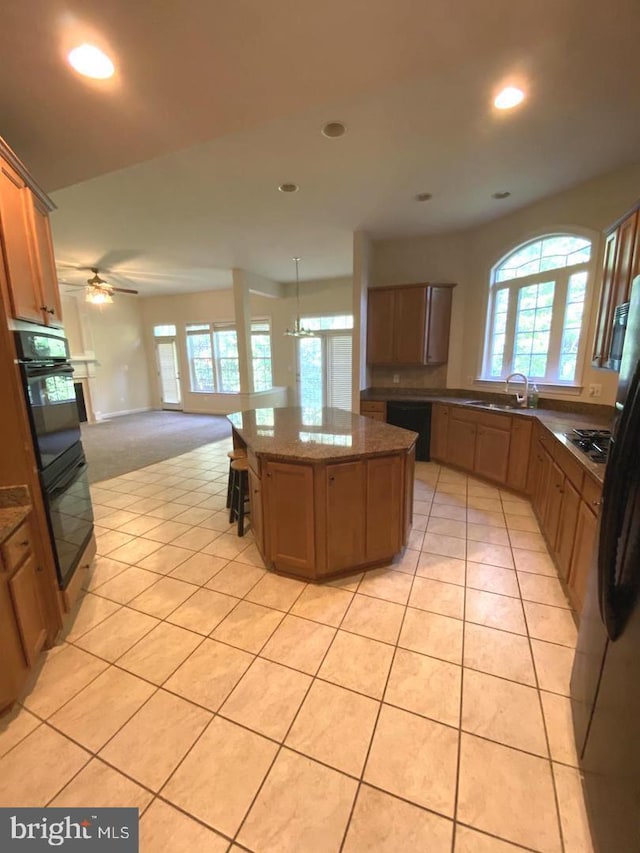 kitchen featuring black appliances, a sink, a kitchen island, open floor plan, and light tile patterned floors