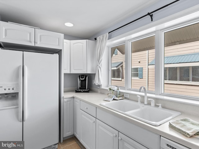 kitchen featuring light countertops, dishwashing machine, white refrigerator with ice dispenser, white cabinetry, and a sink