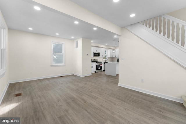 unfurnished living room featuring stairway, recessed lighting, baseboards, and wood finished floors