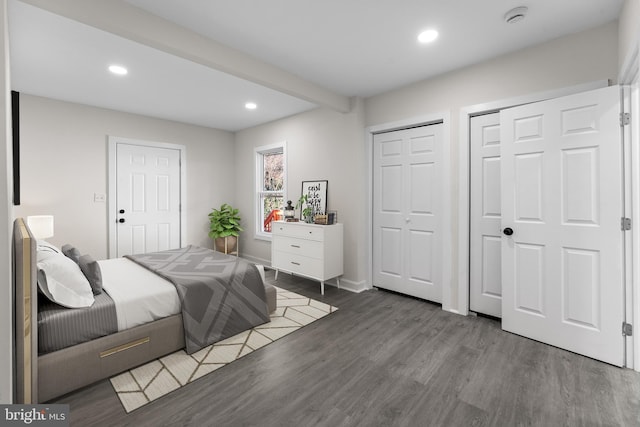 bedroom with two closets, baseboards, beamed ceiling, recessed lighting, and wood finished floors