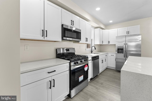 kitchen featuring light stone counters, light wood-style flooring, appliances with stainless steel finishes, white cabinets, and a sink