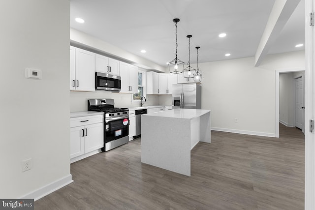 kitchen with wood finished floors, a sink, stainless steel appliances, white cabinetry, and a center island