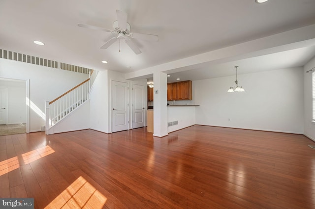 unfurnished living room with visible vents, recessed lighting, stairs, wood-type flooring, and ceiling fan with notable chandelier