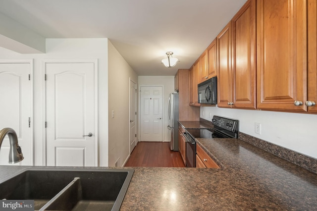 kitchen featuring black microwave, brown cabinets, freestanding refrigerator, electric range, and a sink