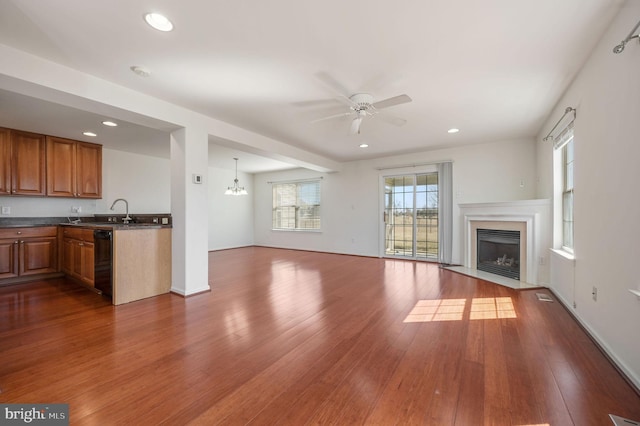 unfurnished living room featuring dark wood finished floors, a fireplace with flush hearth, ceiling fan with notable chandelier, and recessed lighting