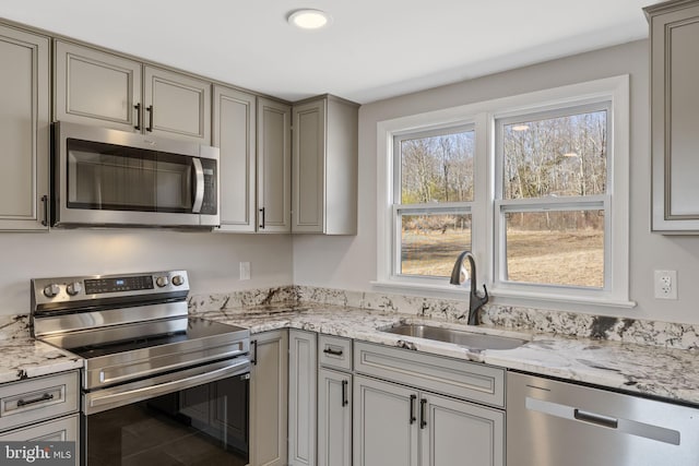 kitchen featuring a sink, light stone counters, appliances with stainless steel finishes, and gray cabinetry