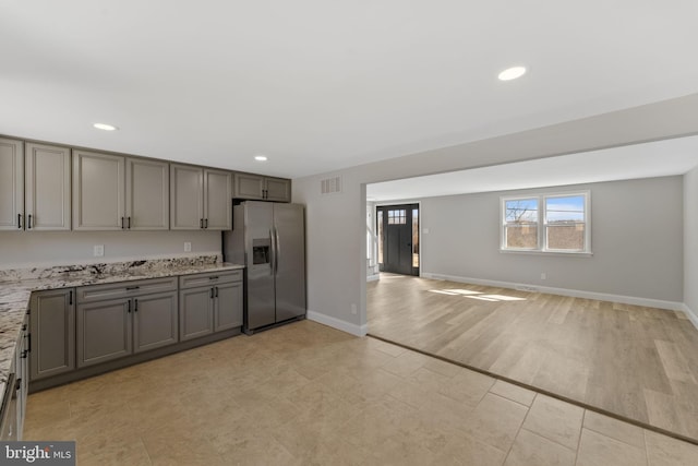 kitchen featuring light stone countertops, recessed lighting, gray cabinets, stainless steel refrigerator with ice dispenser, and open floor plan