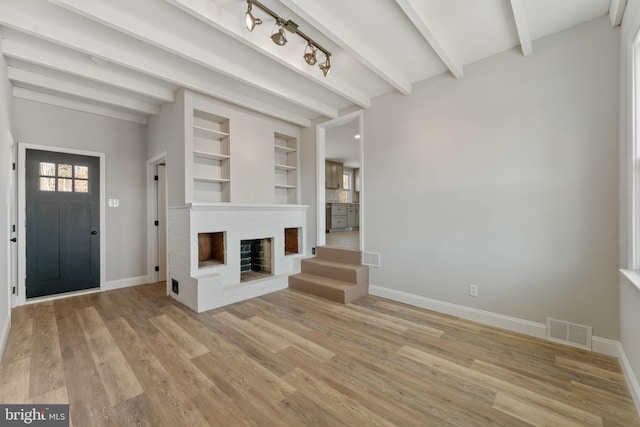 interior space featuring visible vents, baseboards, beamed ceiling, light wood-type flooring, and a fireplace