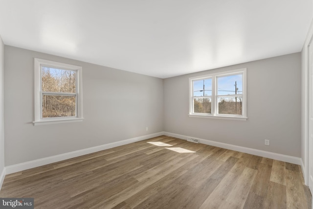 unfurnished room featuring visible vents, baseboards, and wood finished floors