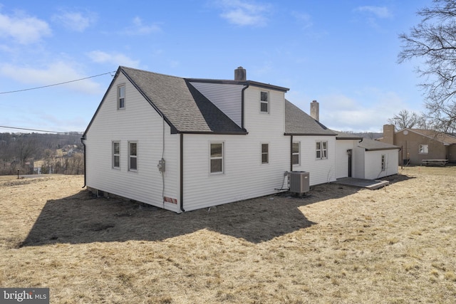 back of house with central AC unit, a chimney, and roof with shingles