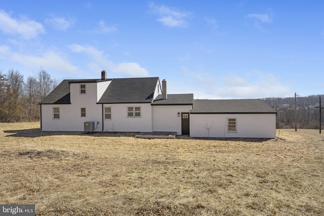 back of property featuring roof with shingles, central AC, and a chimney