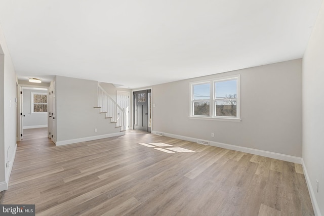 unfurnished living room with stairs, baseboards, and light wood finished floors