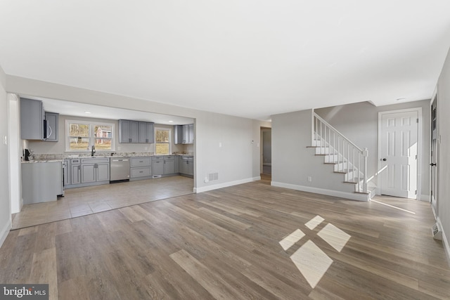 unfurnished living room featuring a sink, light wood-type flooring, baseboards, and stairs