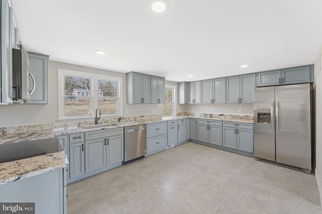 kitchen featuring gray cabinetry, light stone countertops, appliances with stainless steel finishes, and a sink