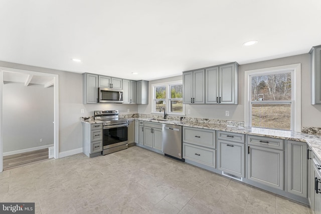 kitchen with light stone counters, baseboards, appliances with stainless steel finishes, and gray cabinets