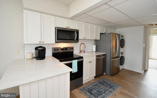 kitchen featuring a sink, decorative backsplash, stacked washer and dryer, appliances with stainless steel finishes, and white cabinetry