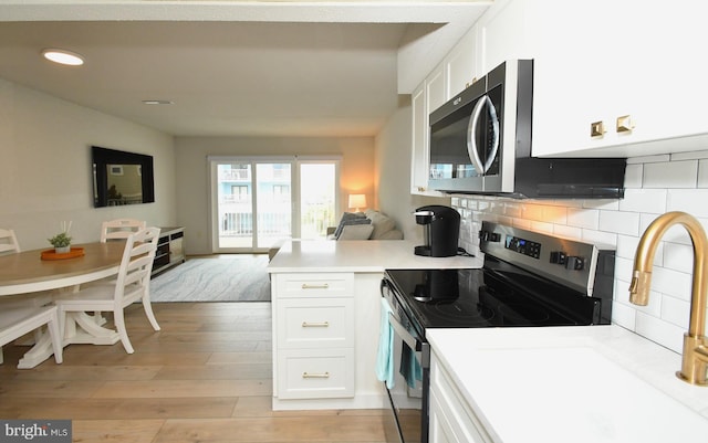 kitchen featuring a peninsula, stainless steel appliances, white cabinetry, open floor plan, and backsplash