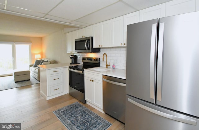 kitchen with a peninsula, a sink, decorative backsplash, stainless steel appliances, and white cabinets