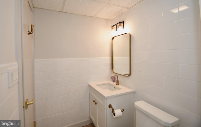 half bathroom with a drop ceiling, toilet, tile walls, and vanity